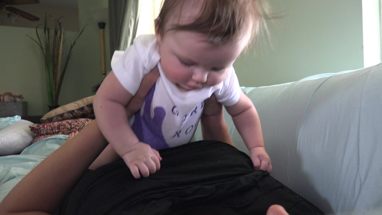 Baby leaning over an adult in a black shirt on a couch.