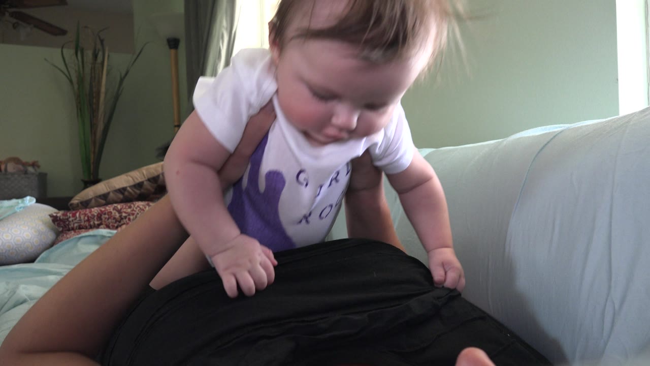 The baby looks downward with both hands near the adult's black shirt, while the couch, pillows, and softly lit wall remain visible in the Westminster home interior.