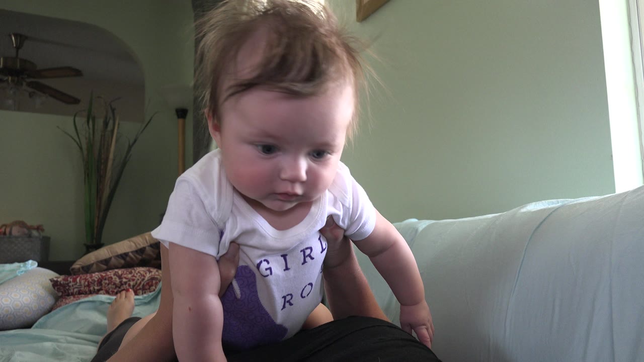 Baby leaning forward on an adult's lap in a living room.