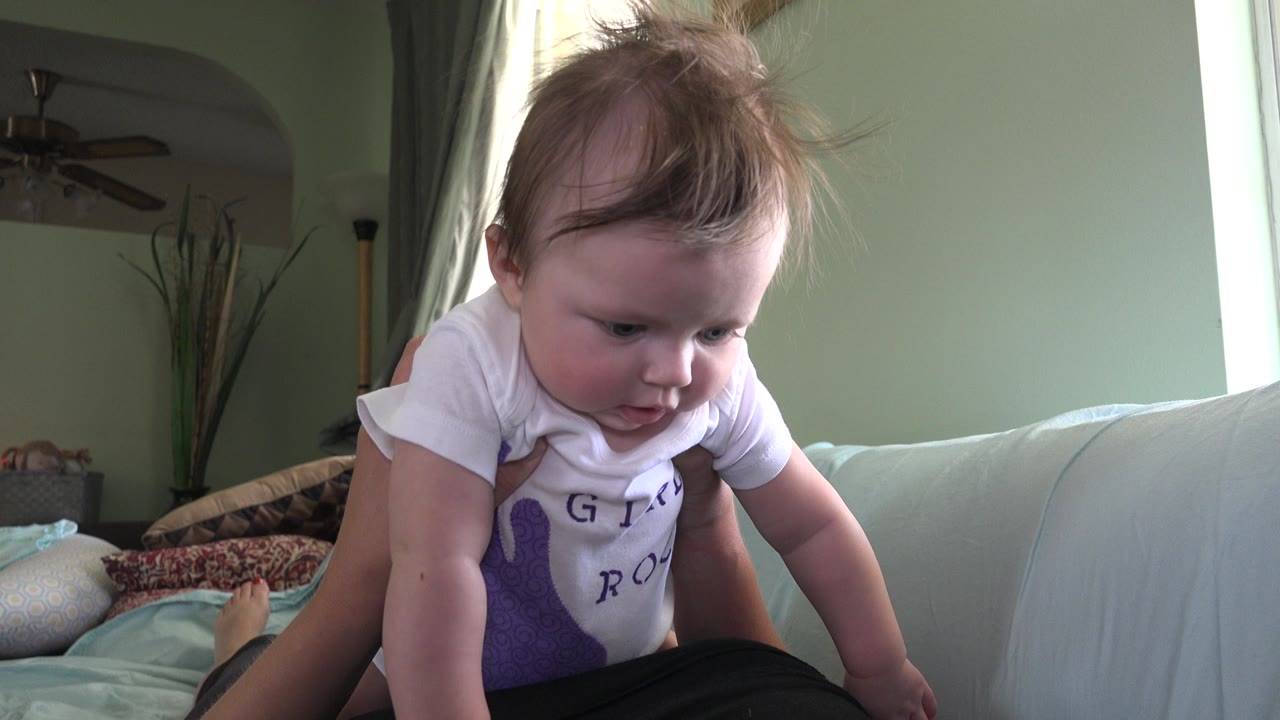 Baby looks downward while held over a sofa.