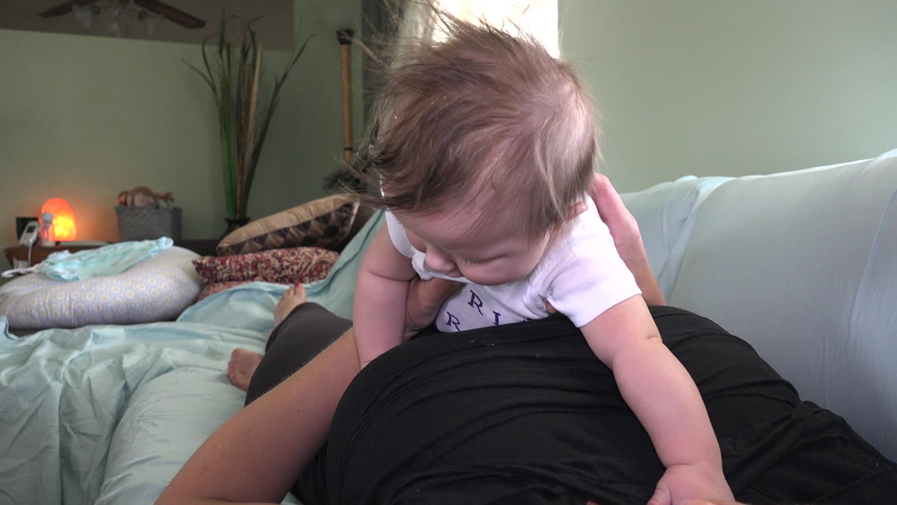 Baby lying across an adult's lap on a bed