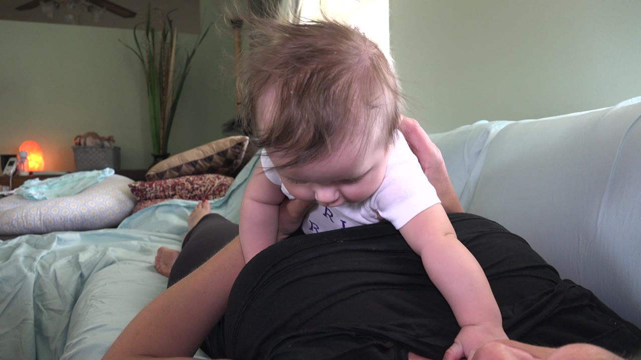Baby leaning forward on a bed over an adult's lap