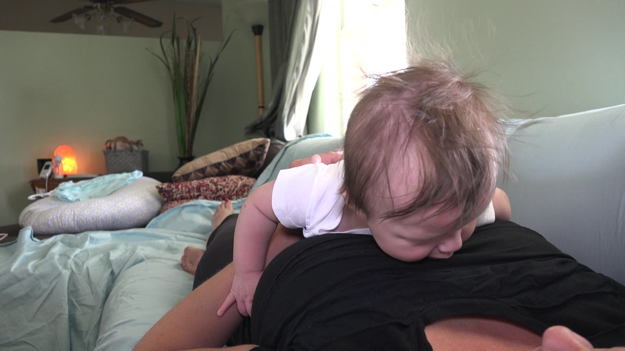 Baby lowering head near an adult's black shirt on the sofa.