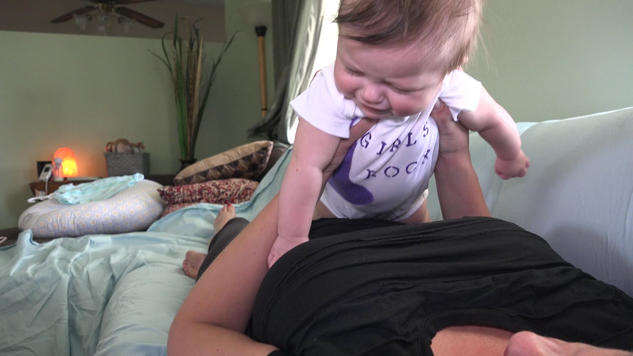 Baby smiling while leaning toward an adult on a sofa.