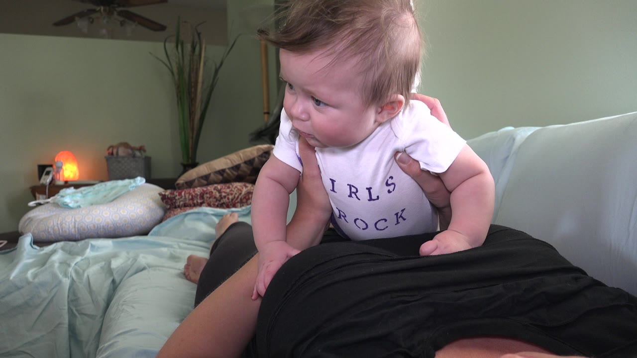 Baby turns slightly while resting on an adult on the couch.