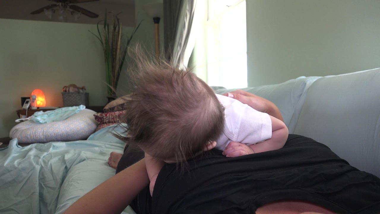 Baby lying on an adult on a sofa in a home interior.