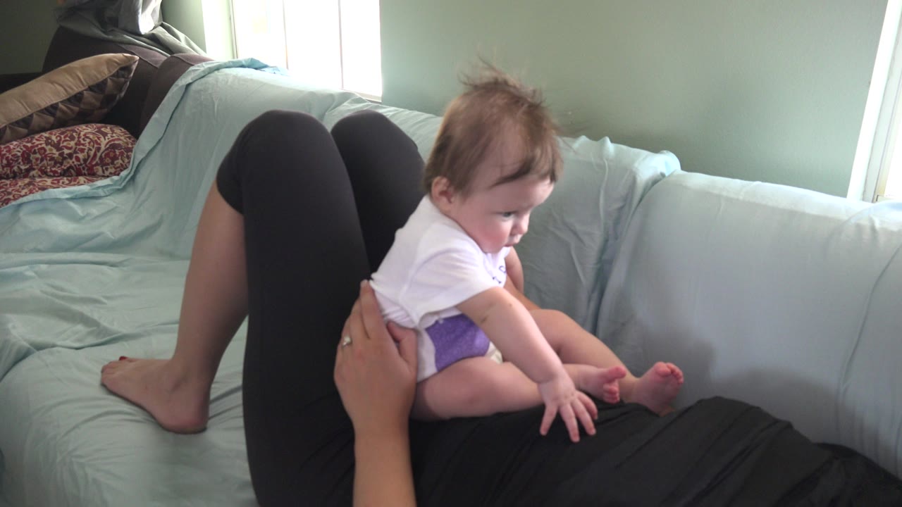 Baby sitting on an adult's legs on a green sofa.