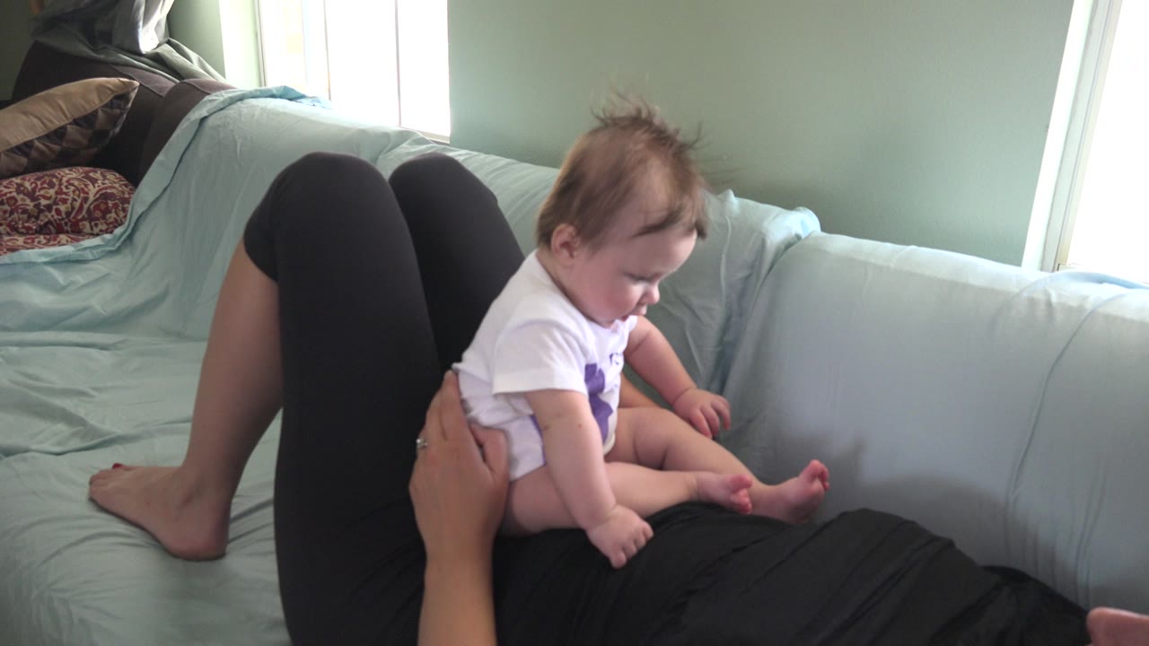 Infant sitting on a person in black clothing on a pale green sofa.