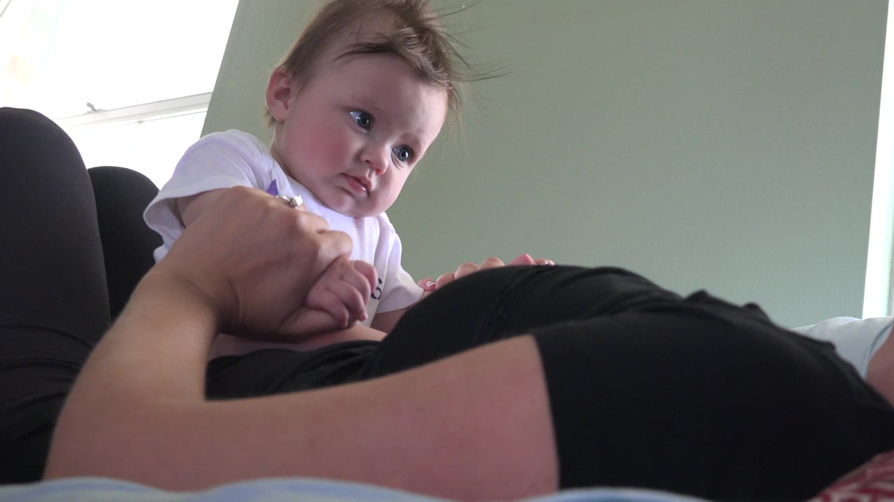 In Westminster, Colorado, the baby remains leaned over the woman's stomach, looking toward the adult hand with window light spilling in from the left.