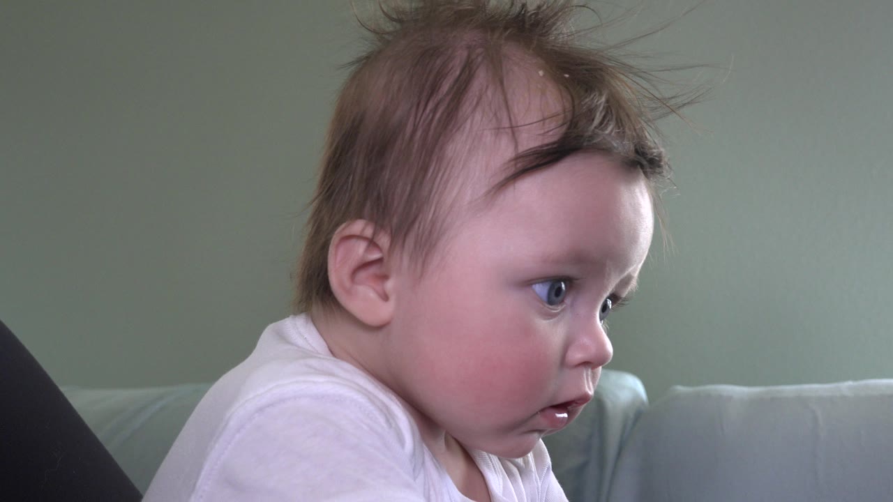 Infant in a white shirt looking to the right indoors.