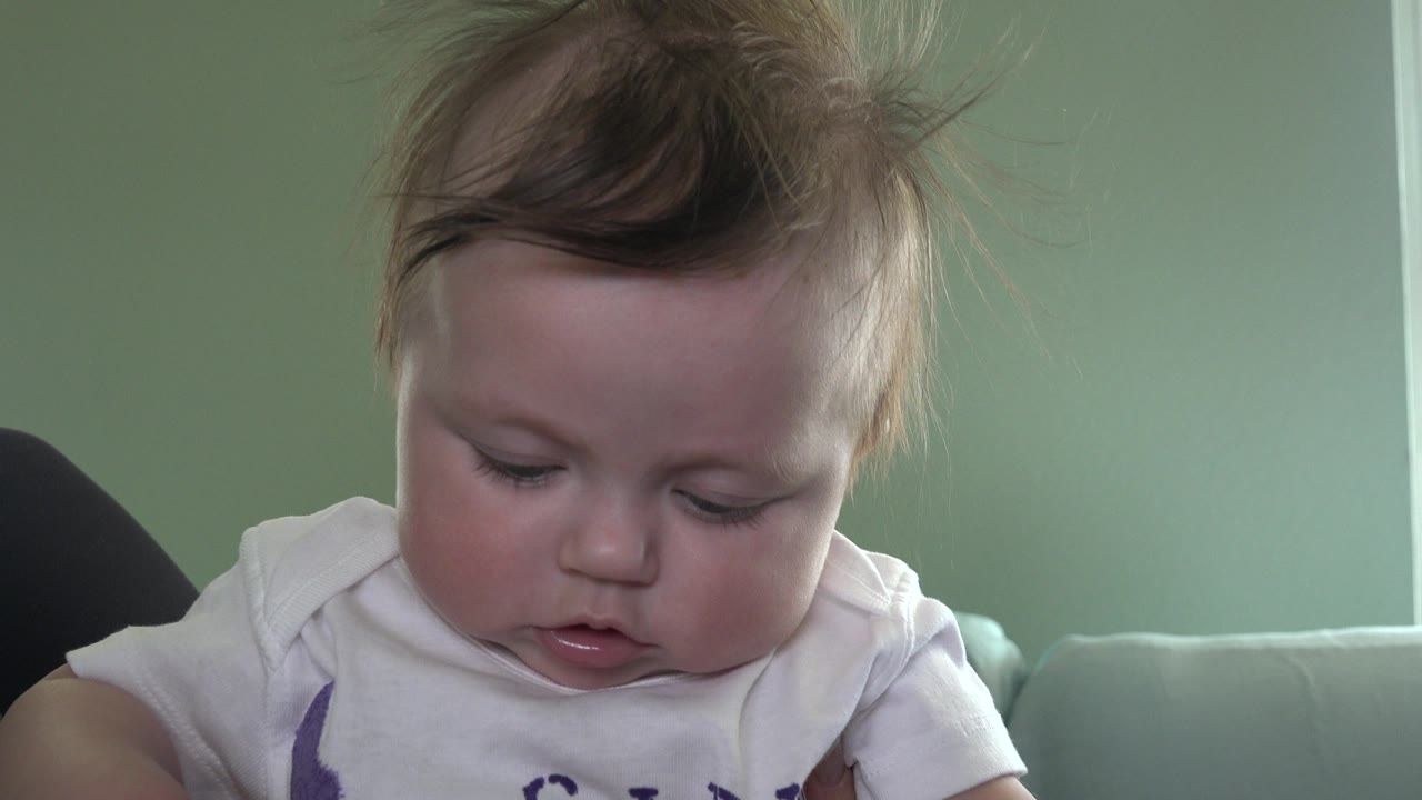 Baby looking down while seated or held against a couch.
