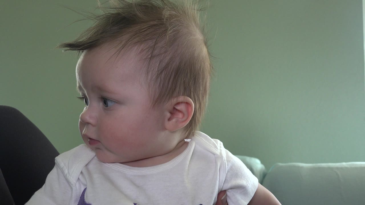 The baby remains turned left in the Westminster, Colorado interior, with tousled hair, soft window-like light, and the sofa edge in the background.