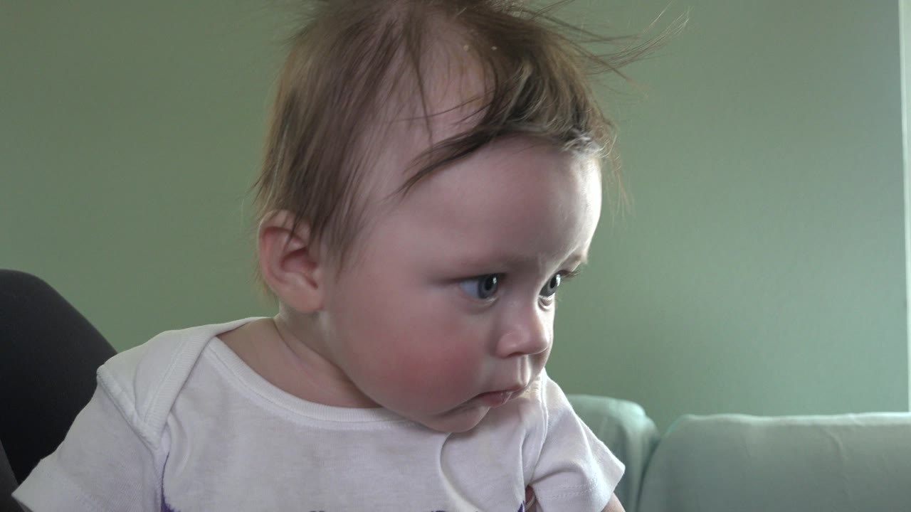 At 0:01, the baby remains close to camera on the couch in Westminster, Colorado, leaning slightly forward while keeping their gaze to the right.