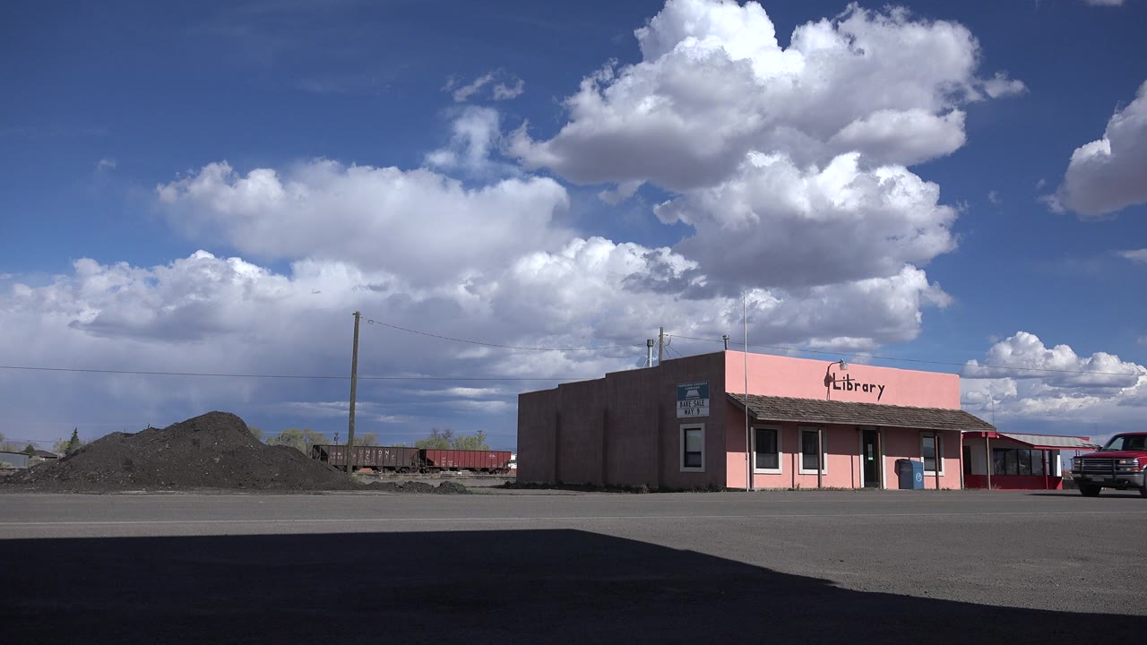 A red pickup begins to enter near the pink library building.