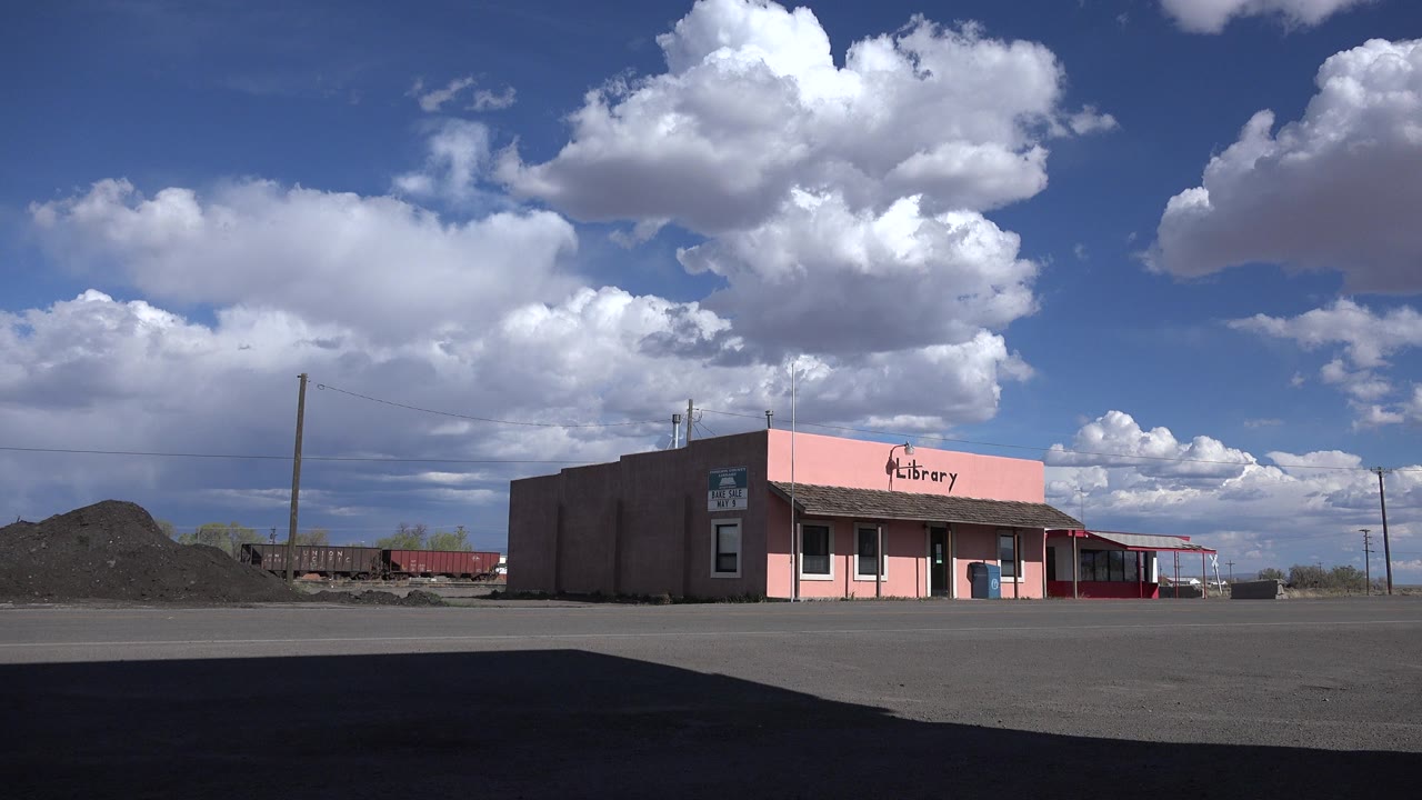 Pink library building across an empty asphalt lot under large clouds.