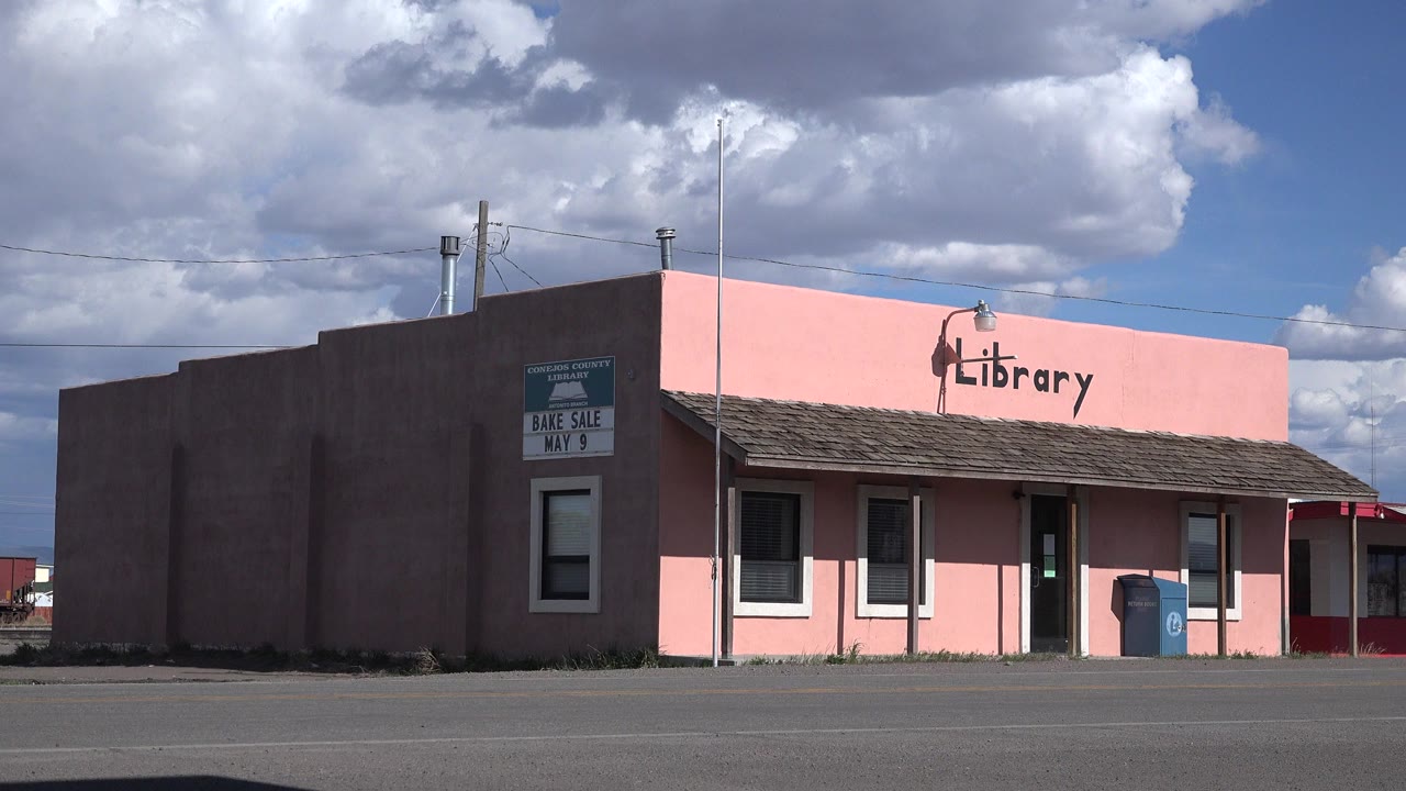 Pink library building across an empty paved road under large clouds.
