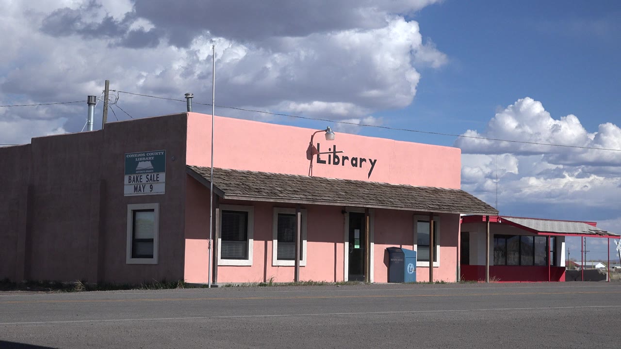 Early frame shows the Sterling, Colorado library facade slightly centered, with the word Library on the pink wall, a blue bin near the entrance, and no visible people.