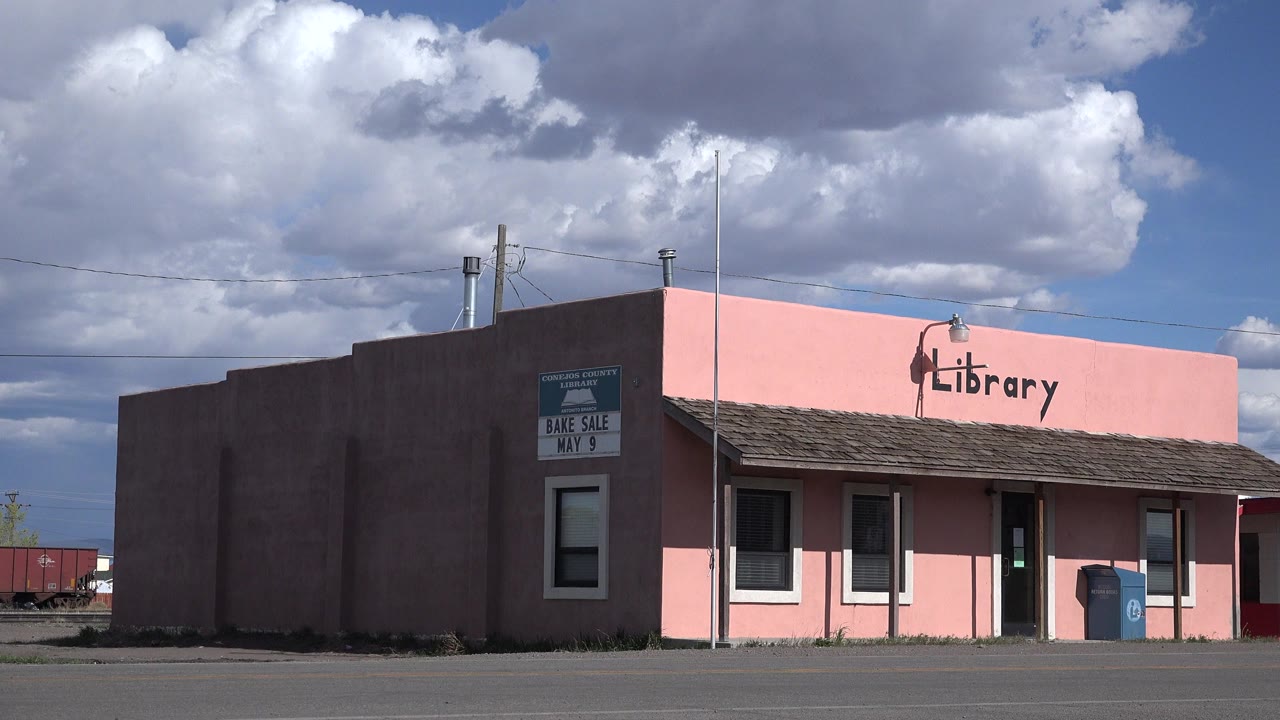 Pink library building beside an empty road under large clouds.