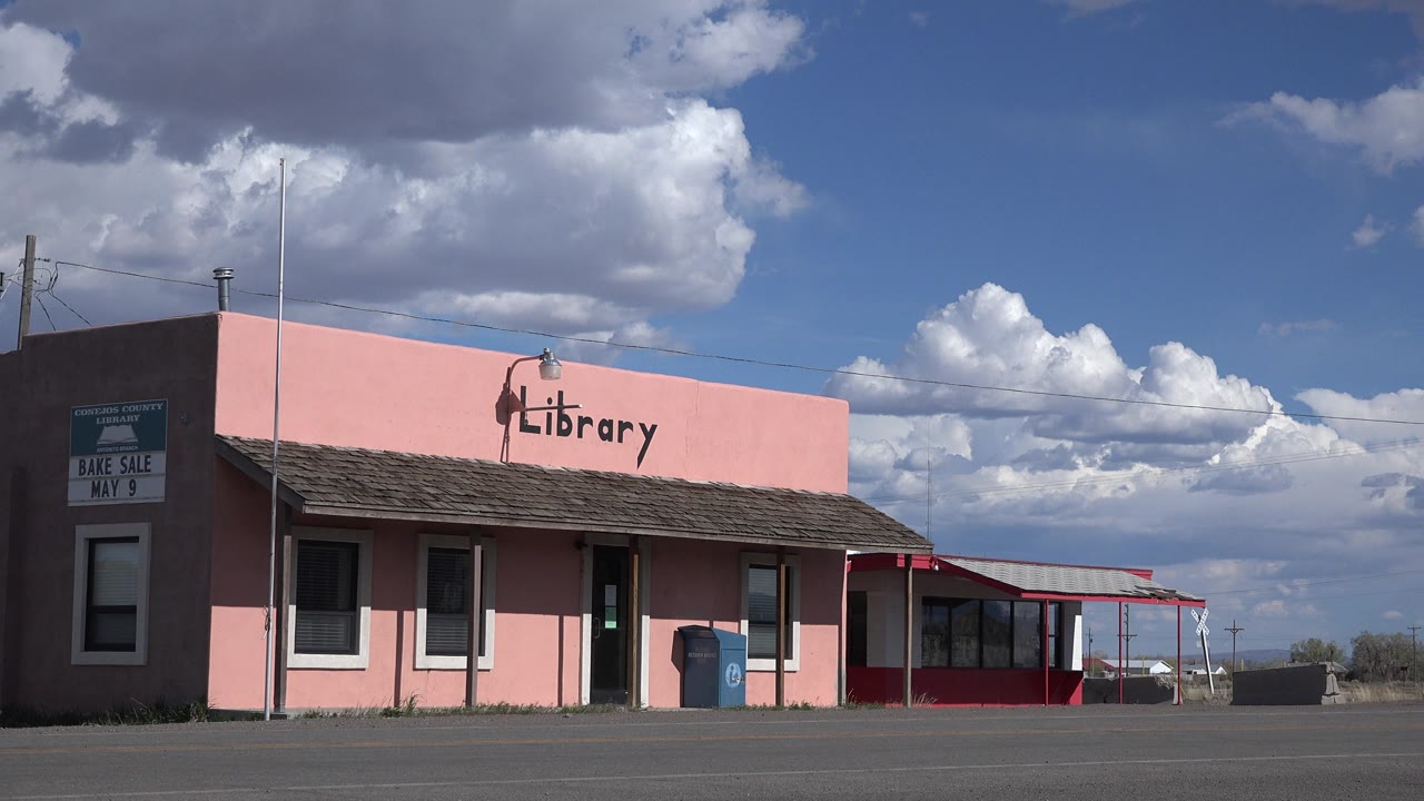 Library building beside a paved road with clouds in the background.