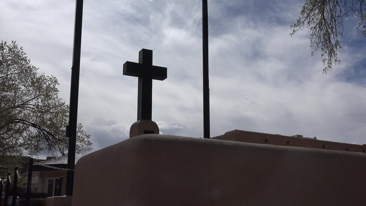 Dark cross above an adobe-colored wall under cloudy sky