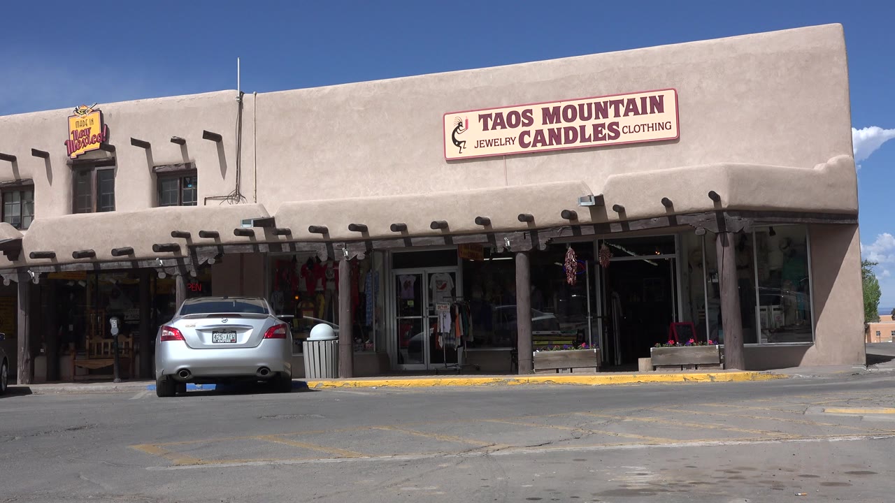 Parked silver car outside Taos Mountain Candles storefronts.