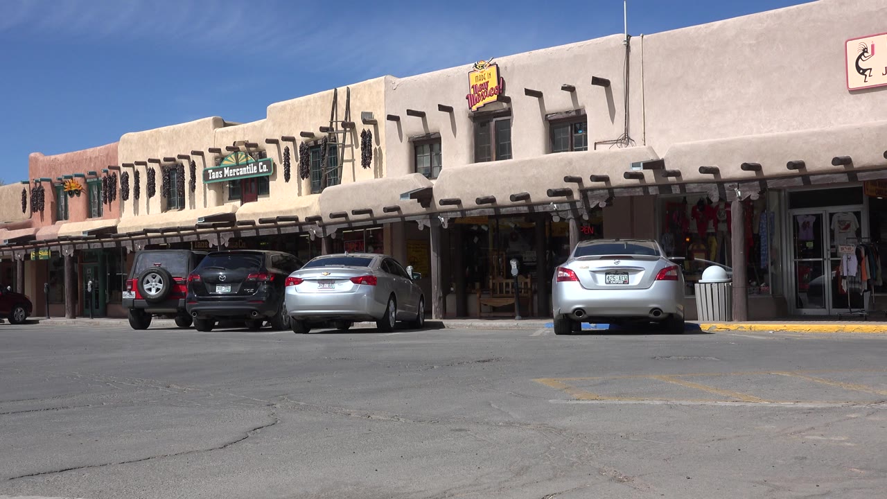 Parked cars outside adobe-style storefronts on a sunny street.