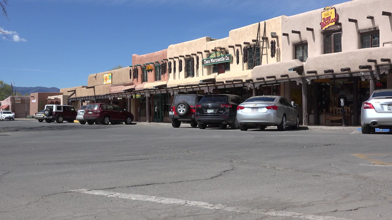 Wide street view of adobe-style storefronts and parked cars