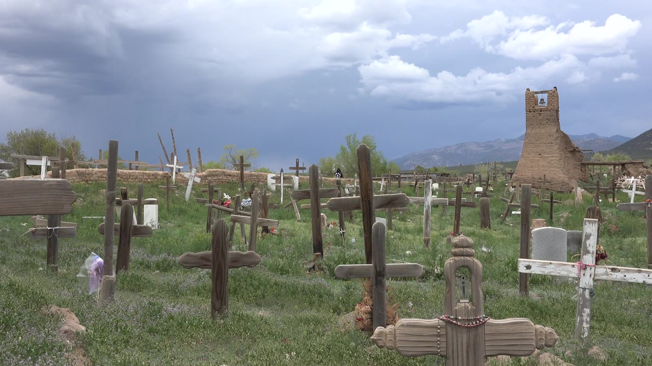 Grassy cemetery with wooden and white crosses under storm clouds.