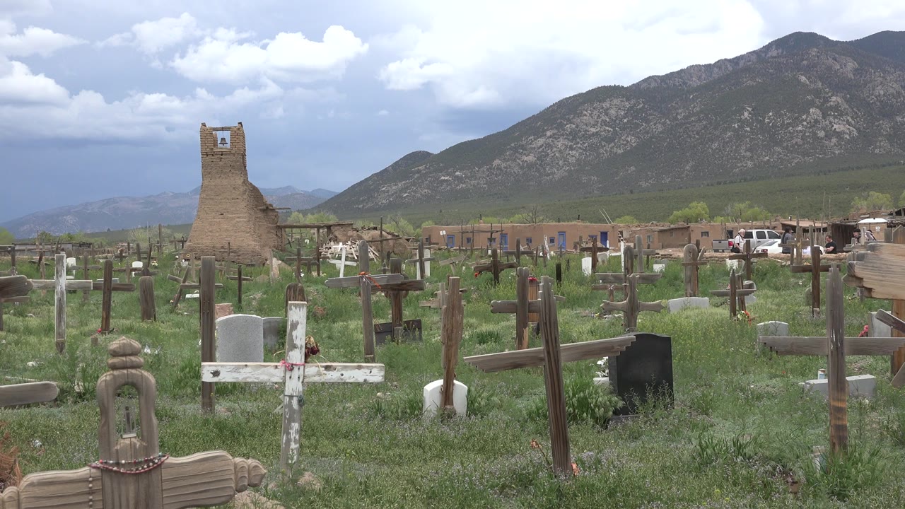 Cemetery crosses and grave markers below a cloudy mountain sky.