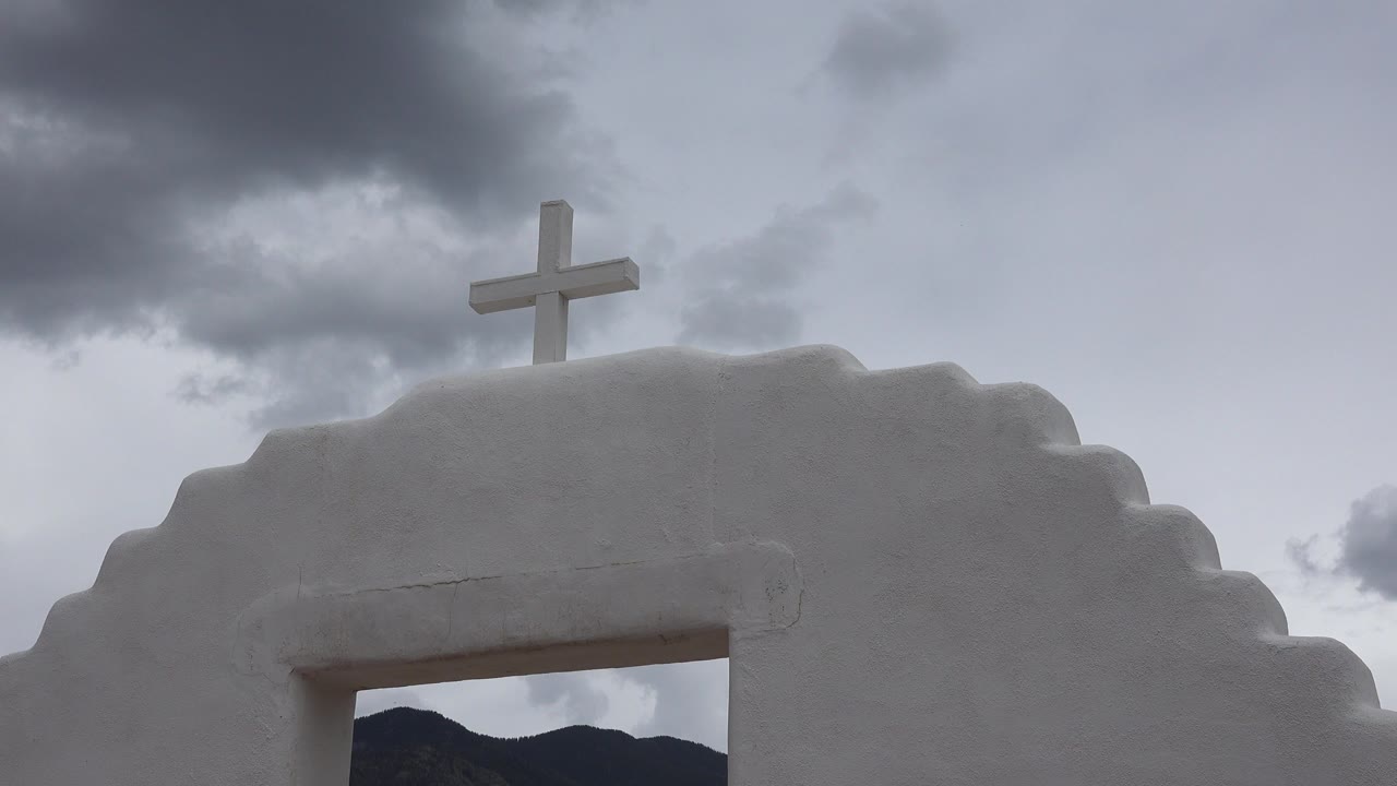 White stepped archway with a cross under gray clouds.