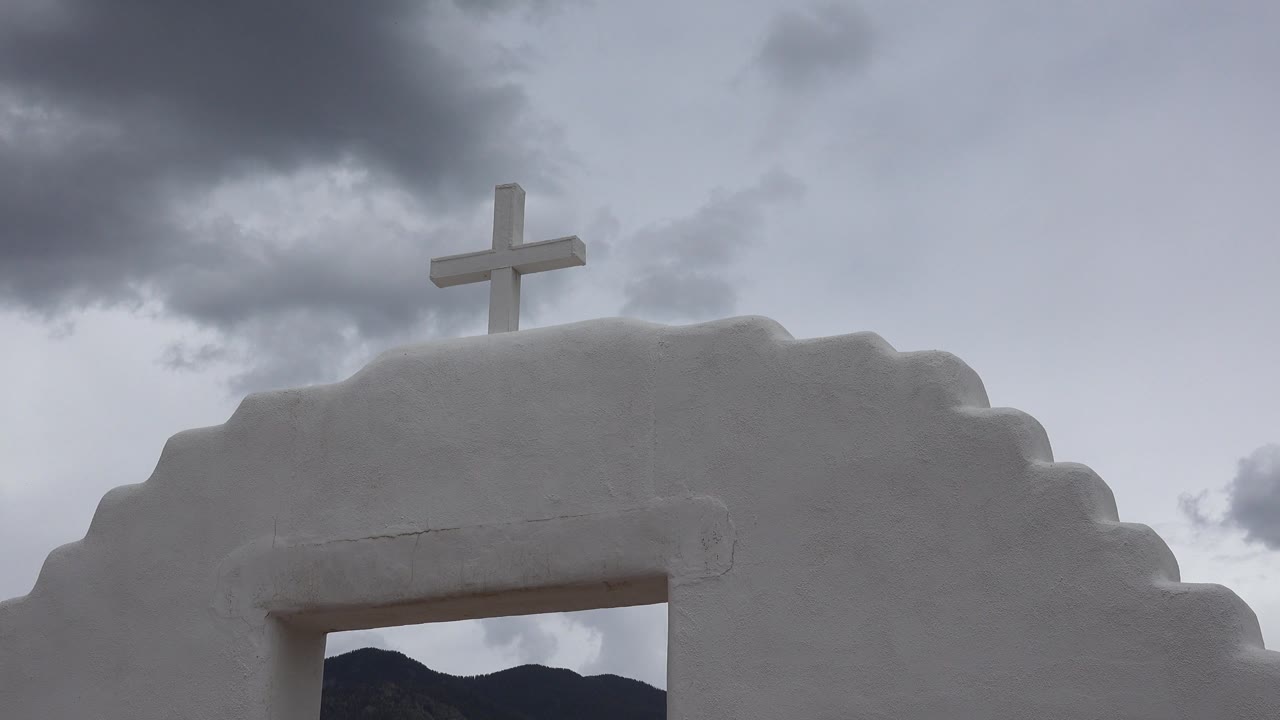 Third frame shows the small cross centered over the white stair-stepped wall in Taos New Mexico, with the arch opening cropped low and no visible people.