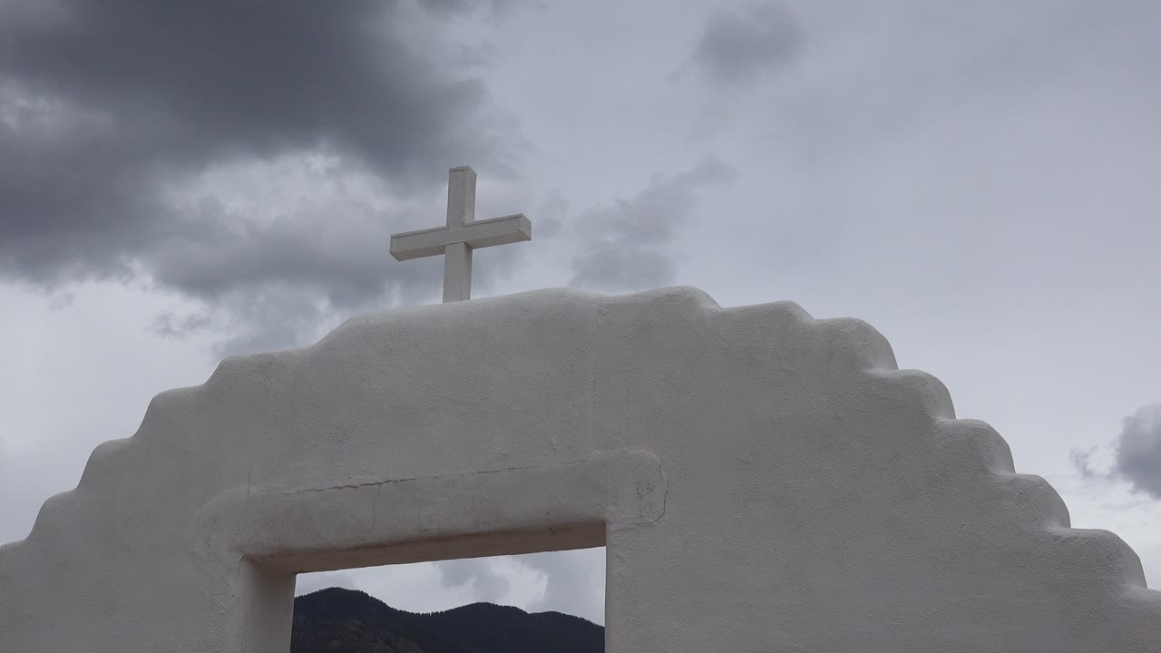 At two seconds, the Taos arch fills the lower half of the frame, with the white cross silhouetted lightly against gray-blue sky and no visible people.