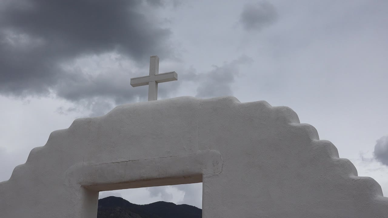 White chapel facade with cross below stormy clouds