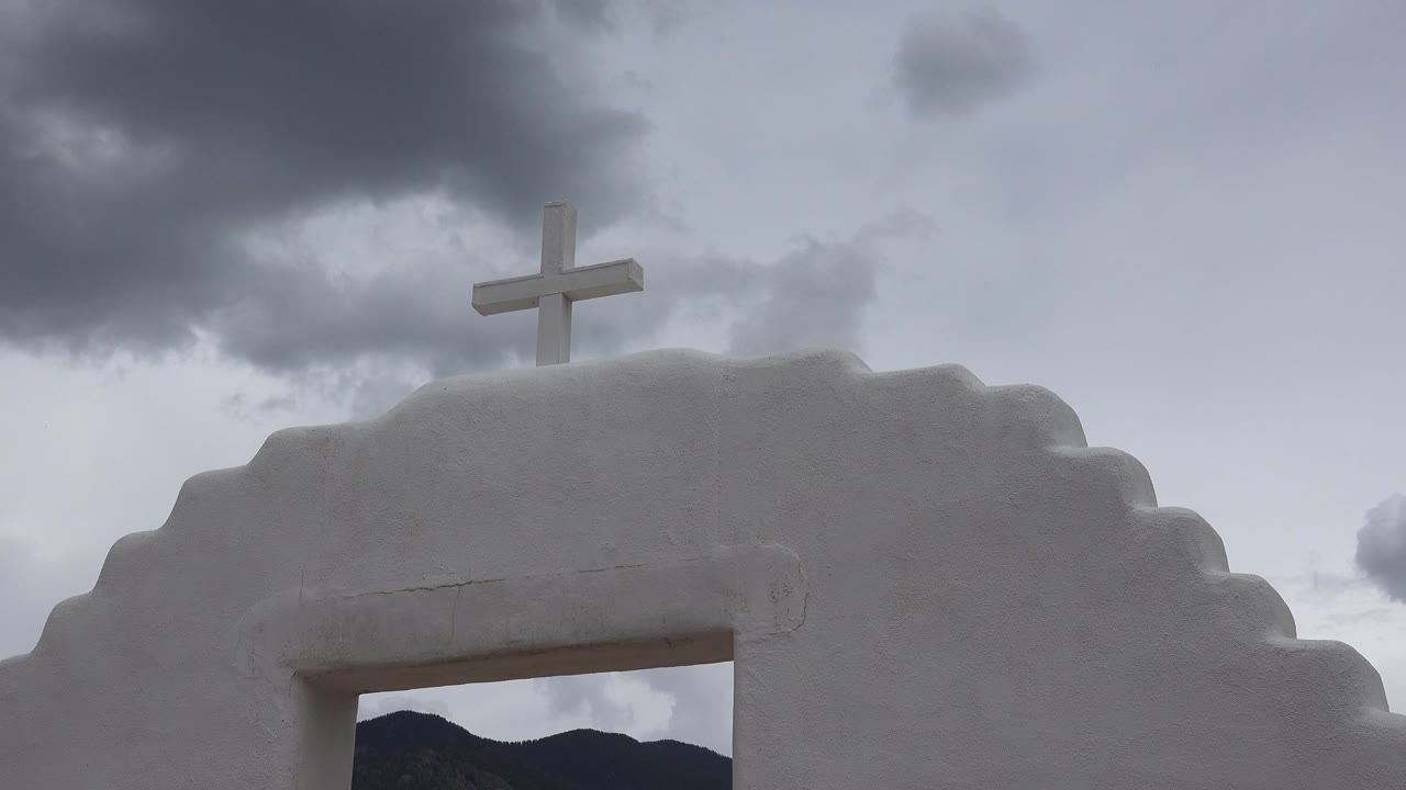 White stepped chapel facade with a cross under dark clouds.