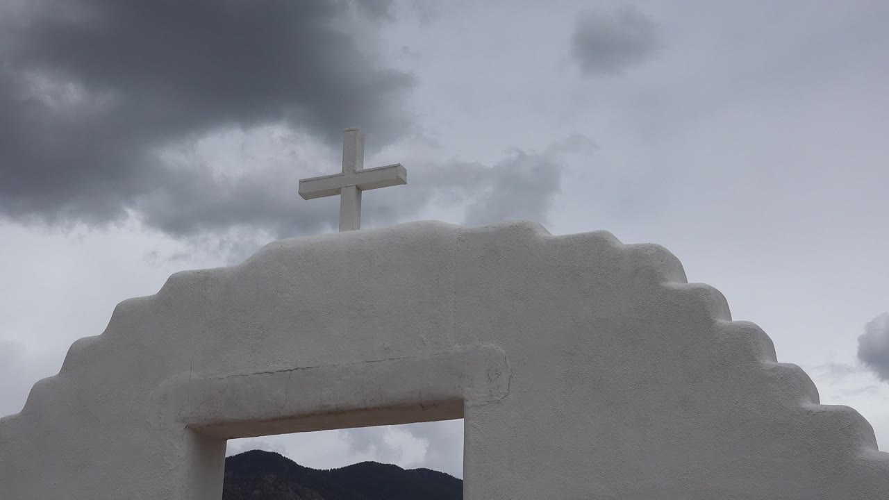 White stepped structure with a cross under gray clouds.