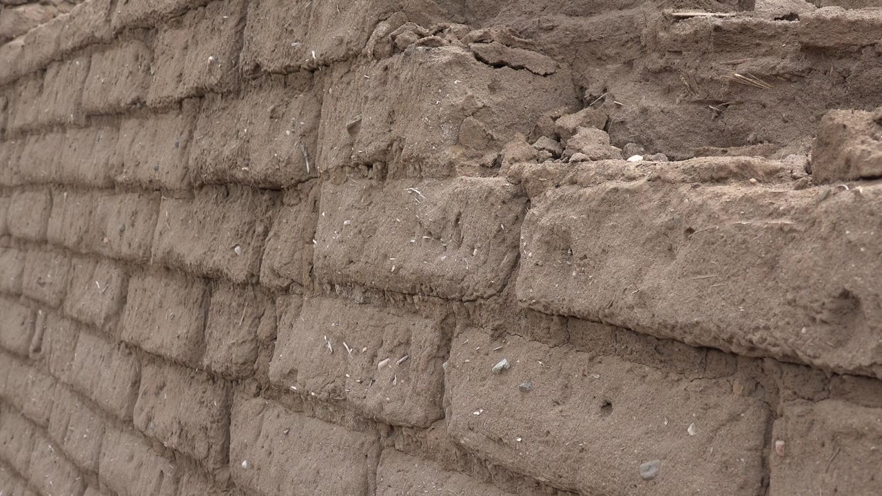 Weathered brown blocks in Taos New Mexico fill the frame, with loose dirt and broken material along the upper edge and no visible people.