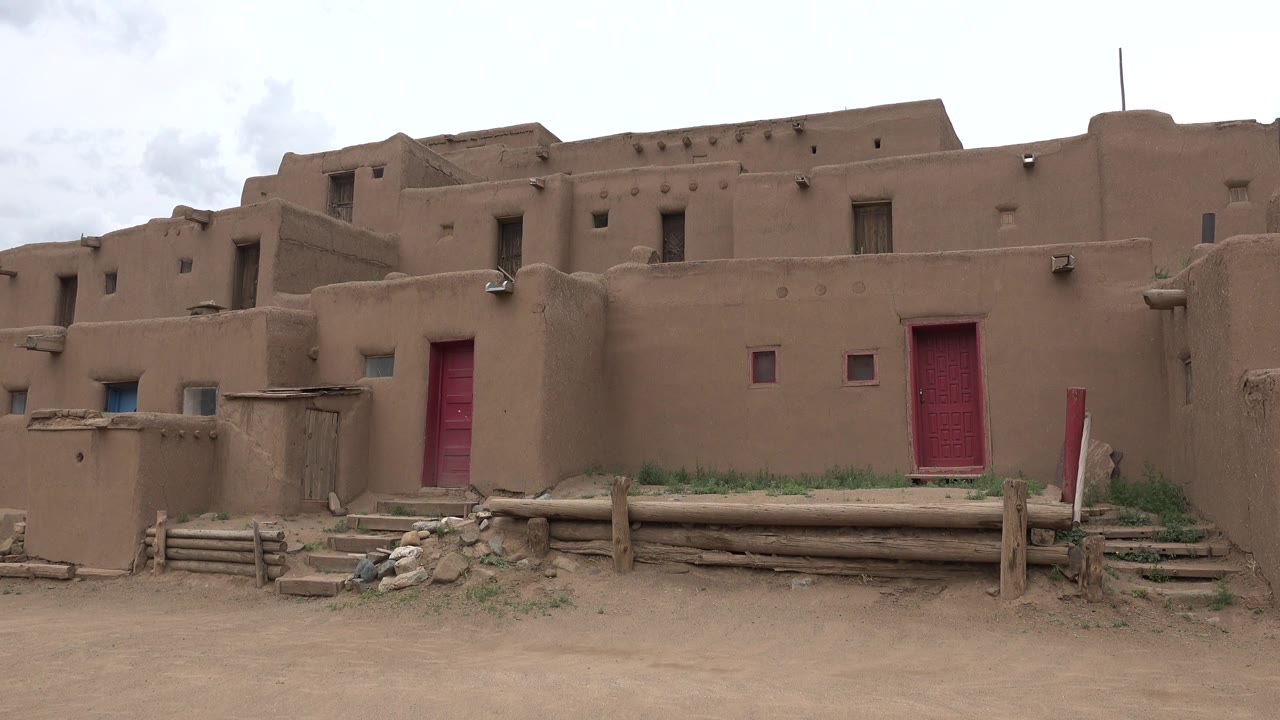 Brown earthen buildings with red doors and a dirt foreground.