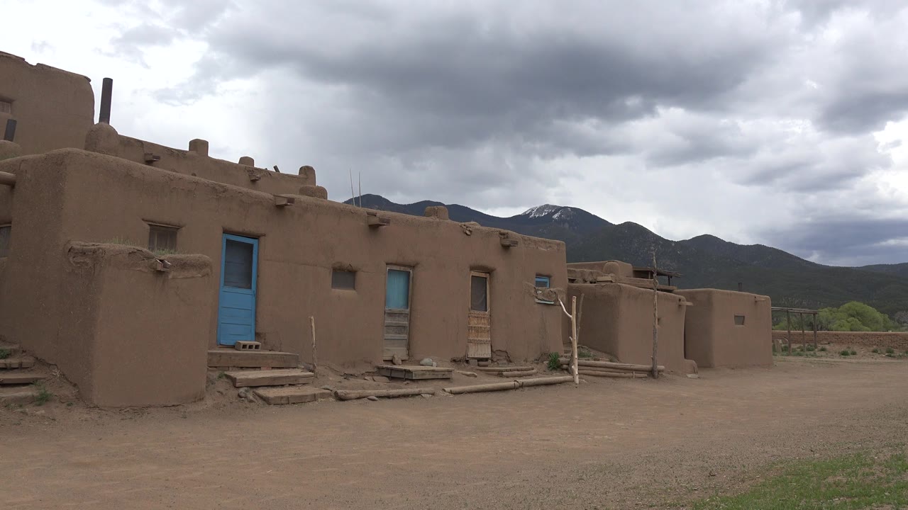 Tan adobe buildings with blue doors below gray clouds