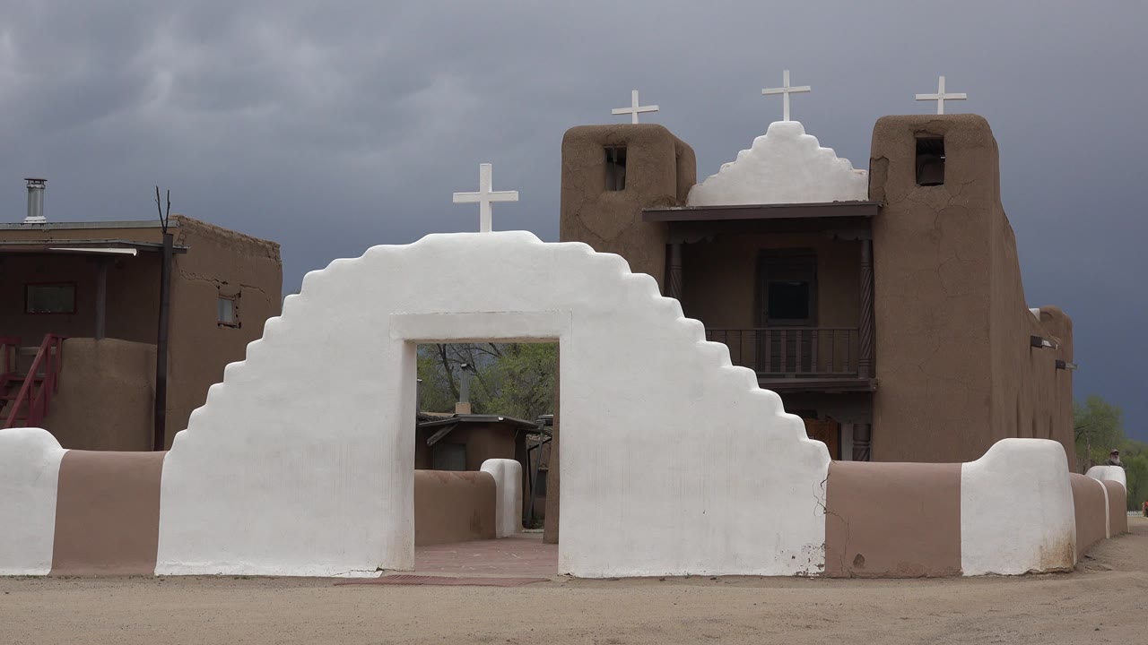 White arched church entry with crosses and brown painted walls under dark clouds.