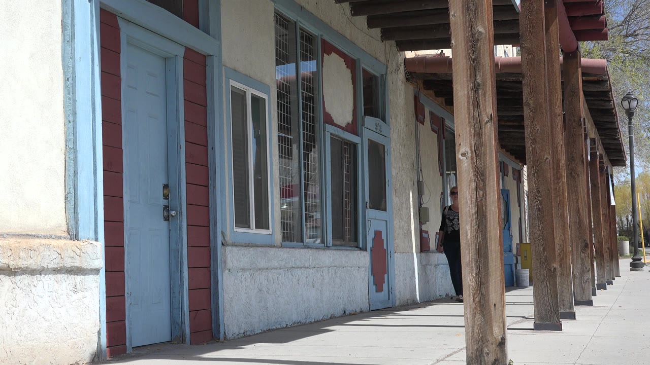 Sunlit sidewalk with blue doors, wooden posts, and a woman partly visible near a storefront.