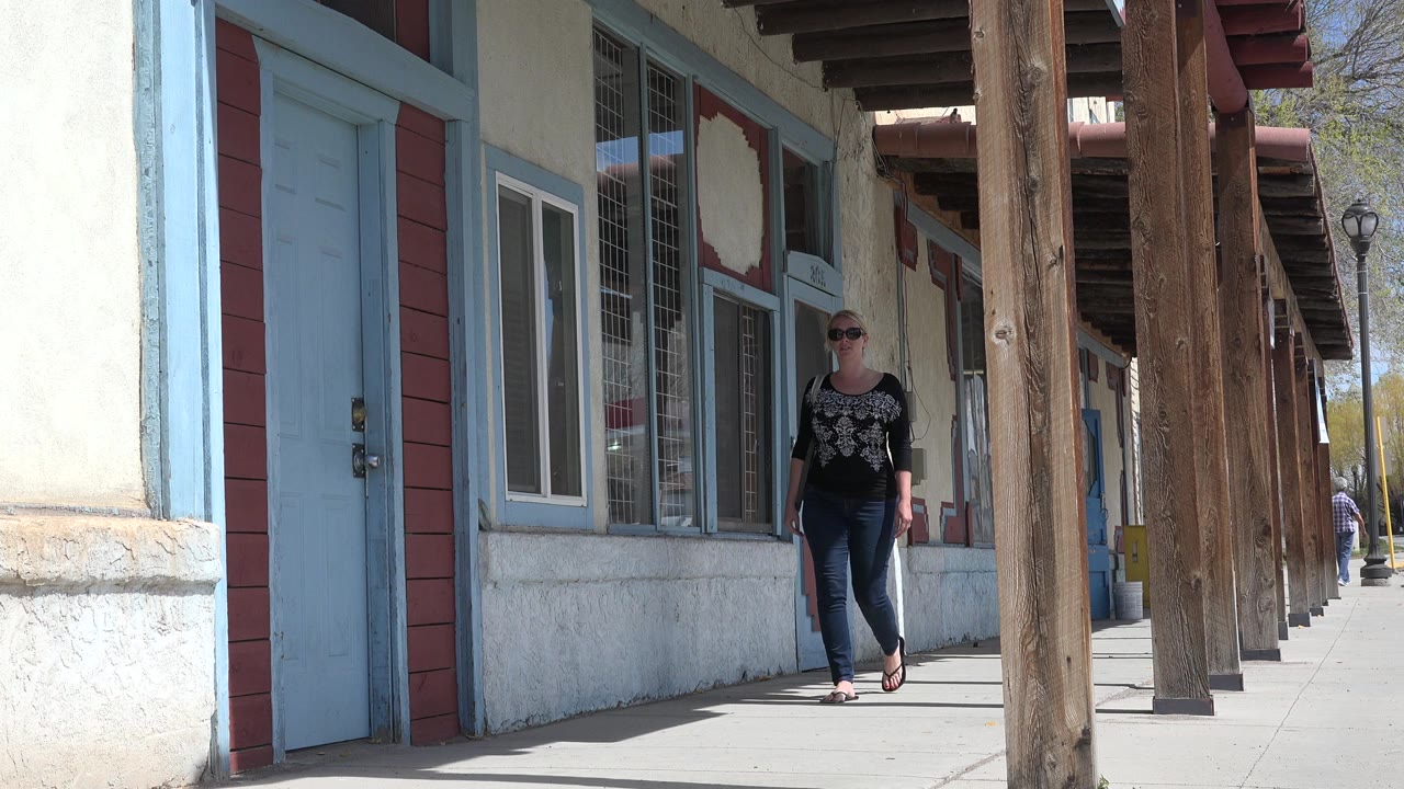 Woman walking on a covered sidewalk beside blue doors and wooden posts.