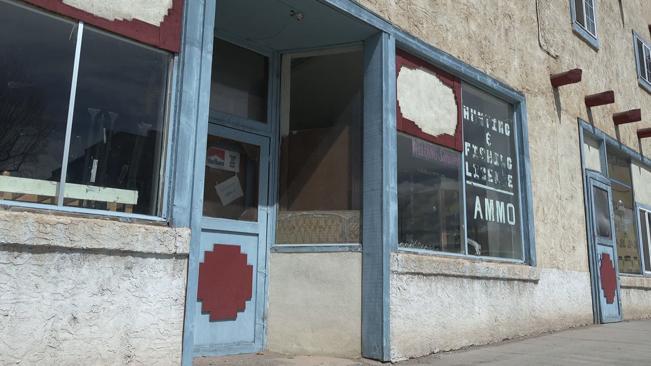 Weathered storefront window and blue-trimmed door on a sunlit sidewalk.