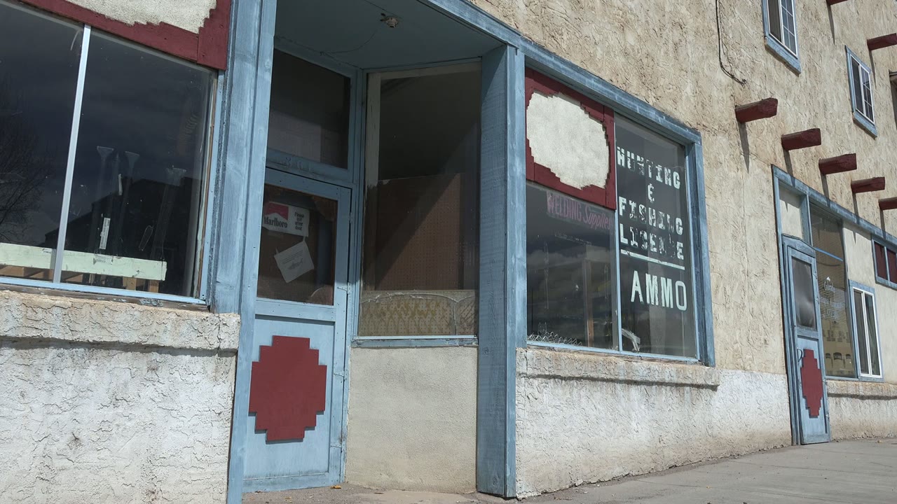 Early pan frame in Taos, New Mexico showing faded storefront lettering, the AMMO window sign area, blue-painted framing, and no visible people.