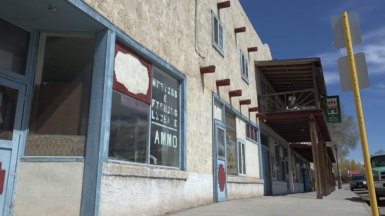 Sunlit stucco storefronts and covered sidewalk beside a street.