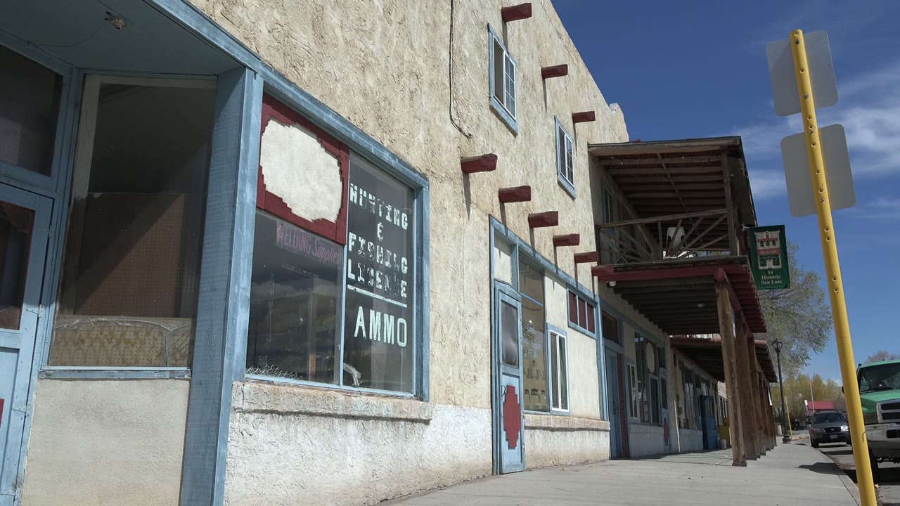 Second moment on the same Taos New Mexico storefront row, showing the painted window text more centrally, the veranda roofline, the sidewalk, and no visible people.