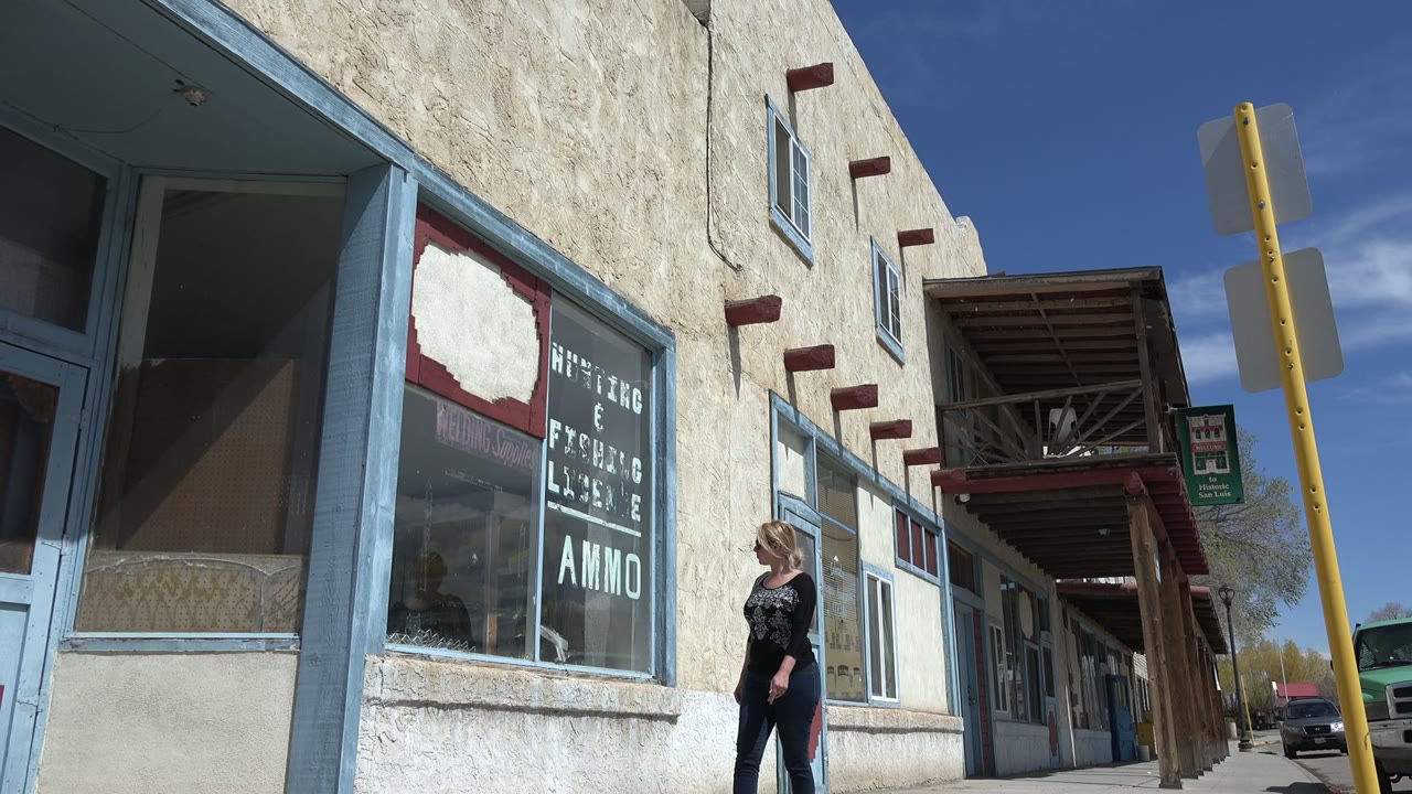 Woman walking near storefront windows on a sunny sidewalk.