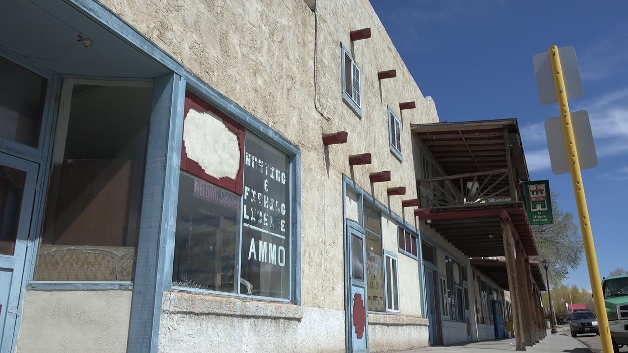 Stucco storefront with blue window trim and a yellow signpost under blue sky.