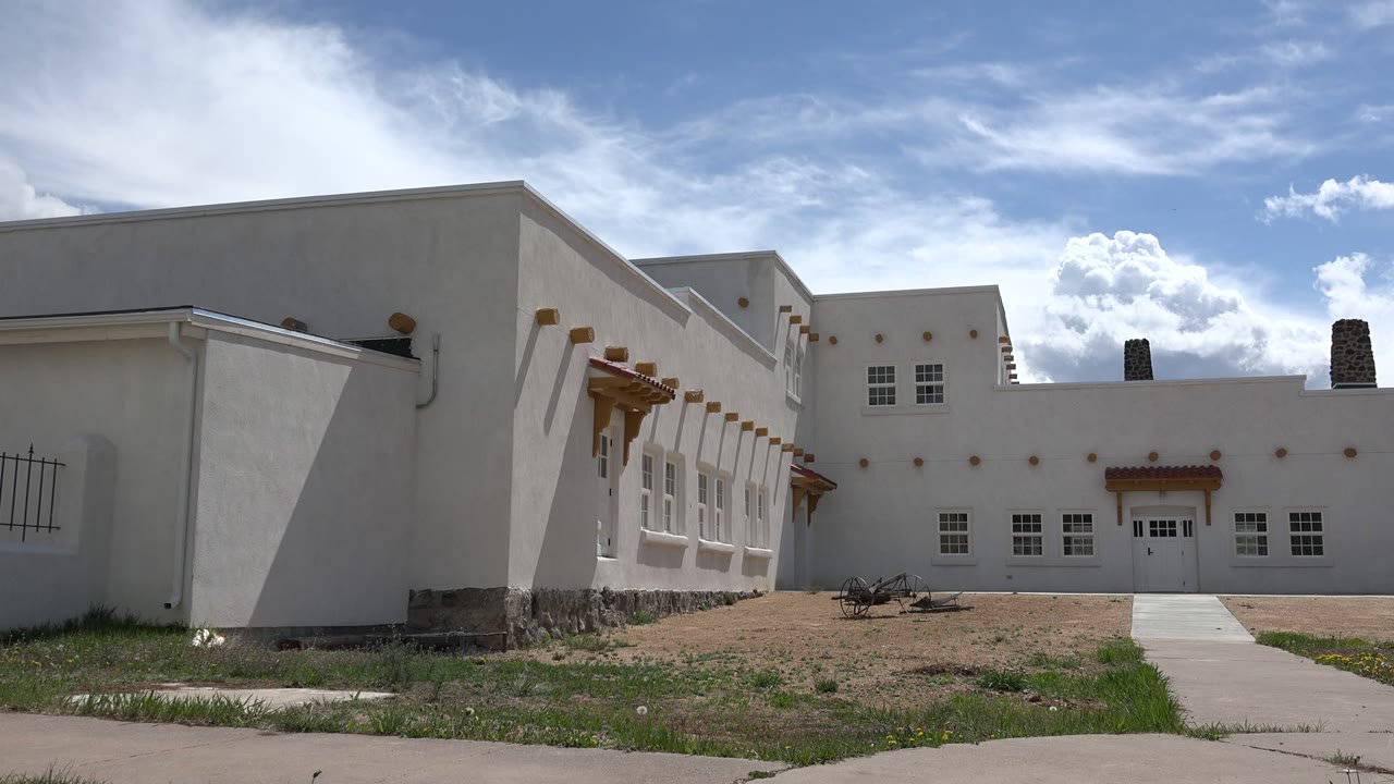 Opening frame of a white stucco building in Taos, New Mexico with square windows, wood shade details, grass at the curb, and no visible people.