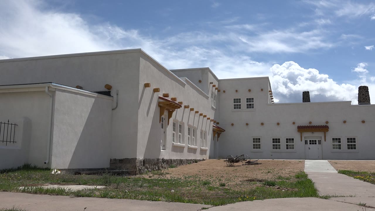Wide view of a white stucco building under blue sky with clouds.
