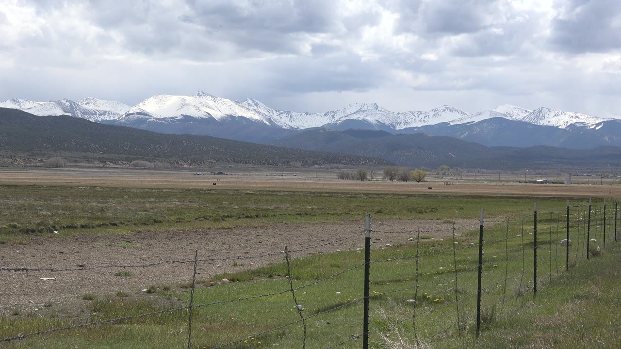 Wire fence and open field with snow-covered mountains in the distance.